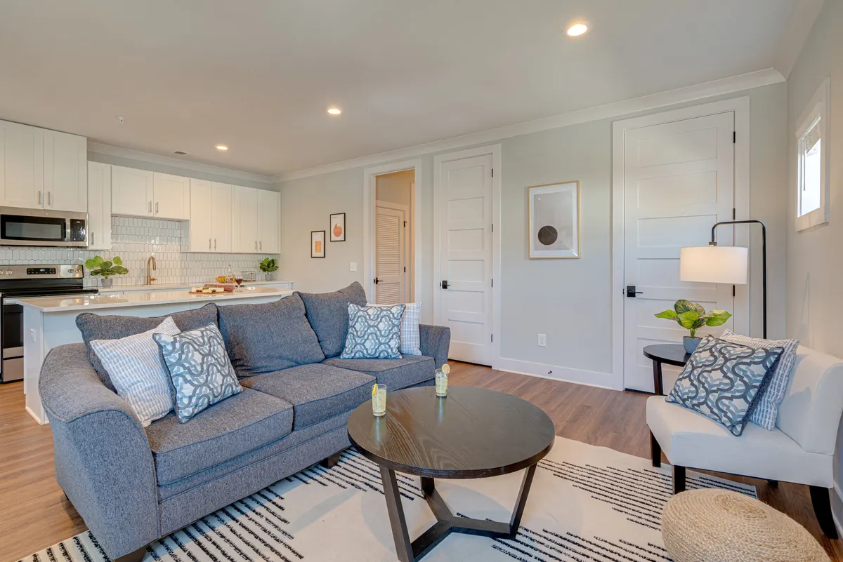The image showcases a warm, inviting living area with a plush sofa adorned with colorful decorative pillows, a stylish coffee table, and an open kitchen area in the background. The scene exudes comfort and is perfect for relaxing, entertaining, or enjoying a cozy meal, all within a thoughtfully decorated urban oasis.