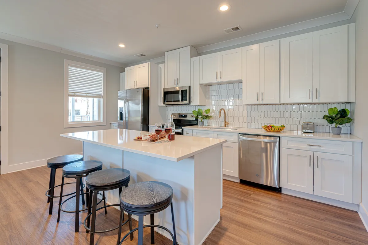 A bright, modern kitchen island with bar stools, gleaming stainless steel appliances, white cabinetry, and touches of greenery. The space feels welcoming and is clearly set up for cooking, dining, and gathering, with everything you’d expect in a well-managed condo.
